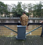 男子不顾危险坐在河边的配电箱上 旁边还有人在钓鱼