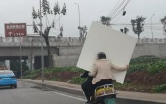 女子手举大板材坐电动车后座 一路摇摇晃晃视线全被挡住